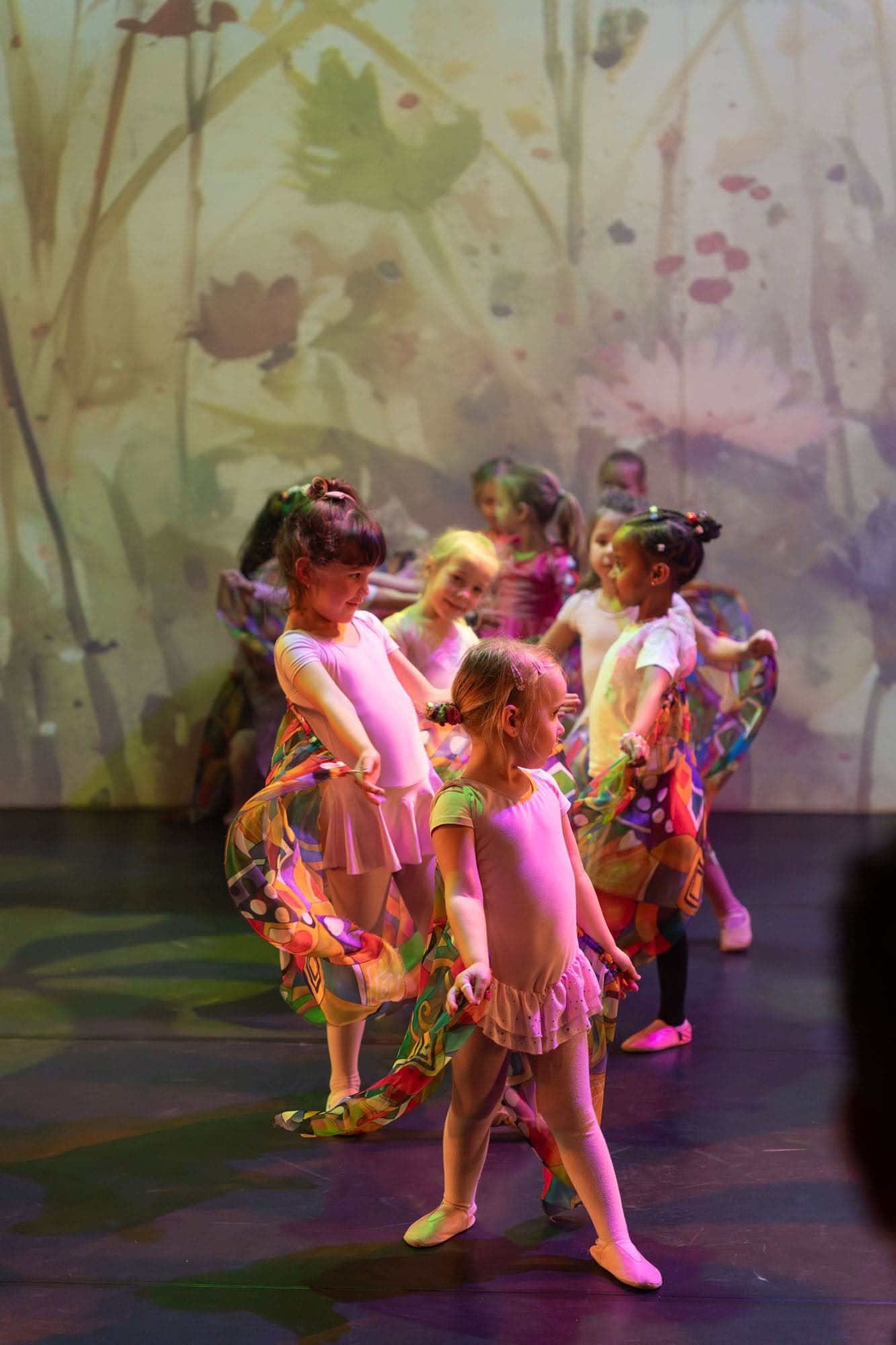 Kleuters in roze balletpakjes dansen op het podium voor een bloemendecor