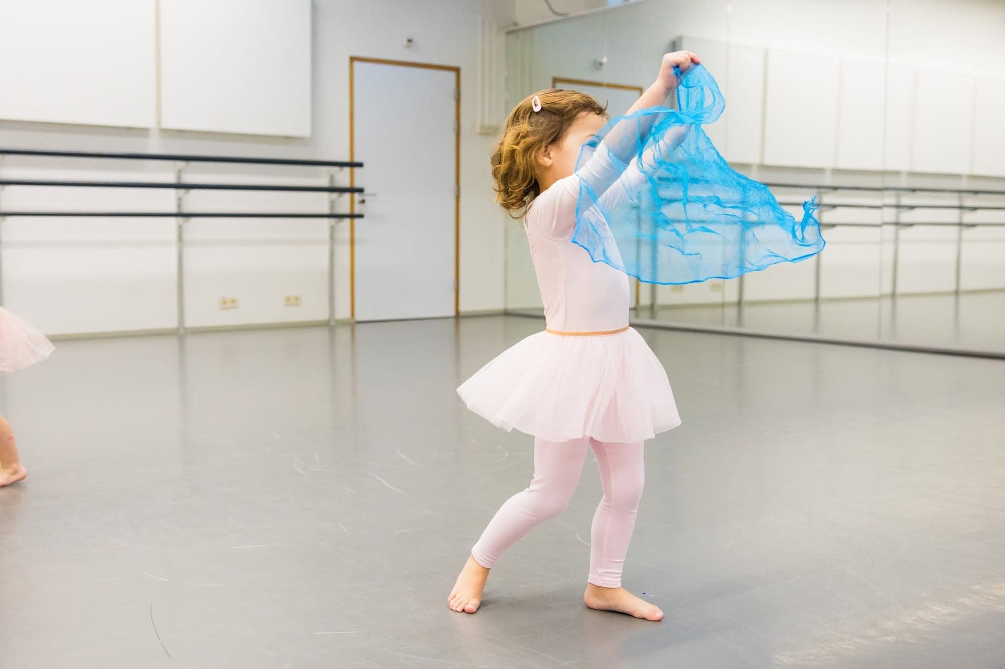 Peuter in een witte tutu danst met een blauwe sjaal in de balletzaal