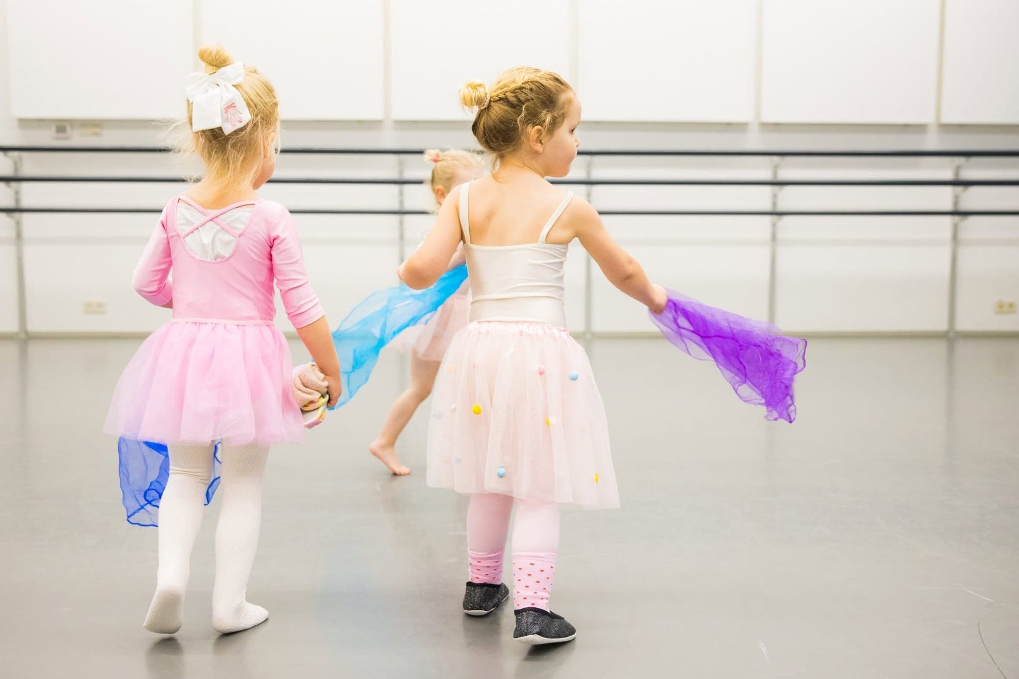 Twee peuters in tutu draaien rond met paarse en blauwe sjaals